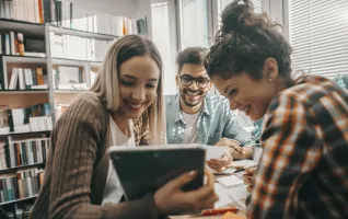 Studierende lernen gemeinsam in der Bibliothek und schauen auf ein Tablet