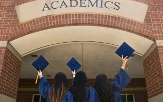 three students holding bachelor graduation caps over academics sign