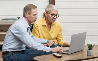 senior man looking through his laptop next to his wife