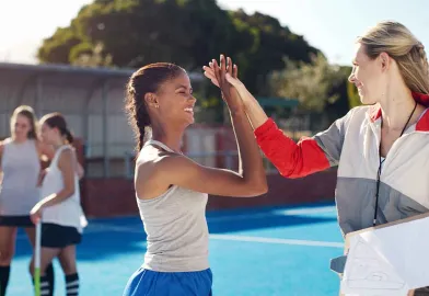 Hockey-Sportlerin und Sozialarbeiterin geben sich High-Five und verknüpfen Soziale Arbeit und Sport