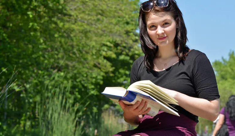 Junge Studentin sitzt mit einem Buch in der Sonne