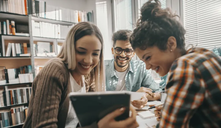 Studierende lernen gemeinsam in der Bibliothek und schauen auf ein Tablet