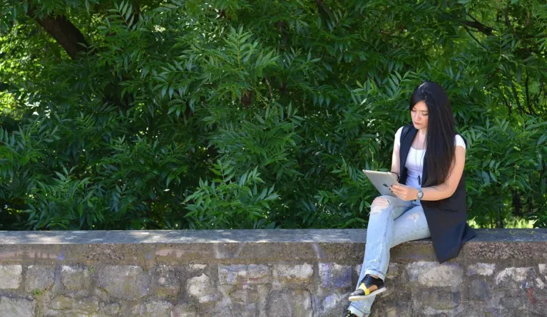 Female student sitting on a wall looking for jobs in Germany using an Ipad