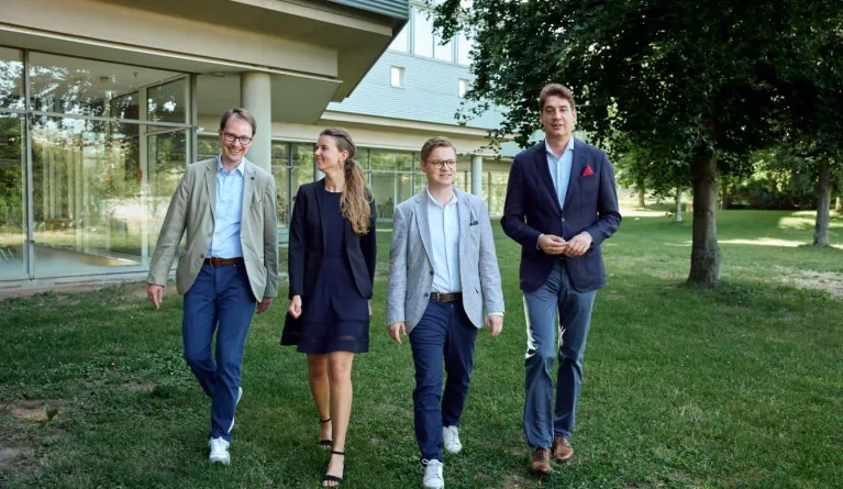 Das Team des Zentrums für Entrepreneurship, bestehend aus vier in dunkelblau gehaltener Business-Kleidung gekleideter Personen, läuft freundlich lächelnd auf die Kamera zu.