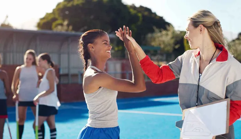 Hockey-Sportlerin und Sozialarbeiterin geben sich High-Five und verknüpfen Soziale Arbeit und Sport
