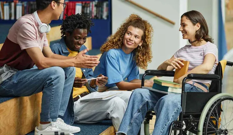 Studentin im Rollstuhl redet fröhlich mit Kommilitonen im Studium mit Behinderung