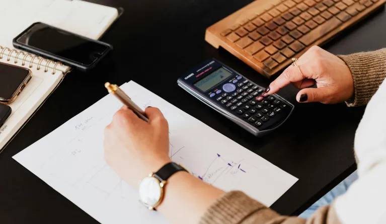 Accountant using calculator and writing numbers down on paper