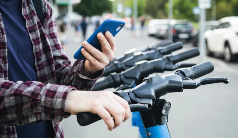Close-up of a man using mobile app to rent electric scooter sustainable mobility