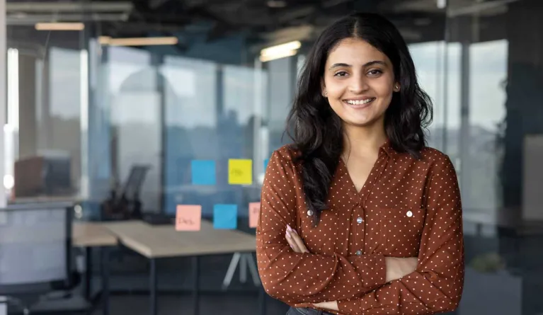 Junge Frau mit schwarzen Haaren lächelt in einem Business-Setting, nachdem sie die Karrieremöglichkeiten nach dem PFH-Fernstudium genutzt hat