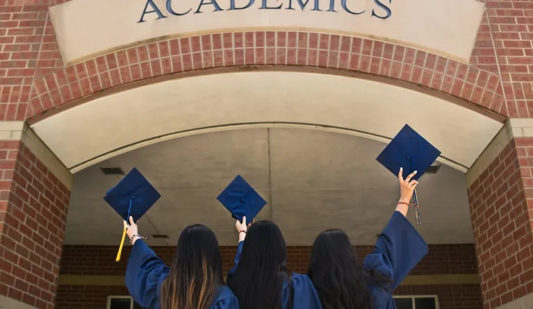 three students holding bachelor graduation caps over academics sign