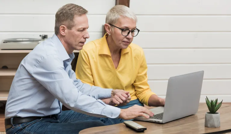 senior man looking through his laptop next to his wife