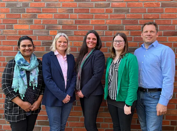 Das Team der Studienkoordination der PFH Stade steht vor einer roten Backsteinmauer.