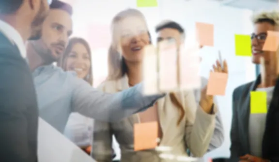 Studierende im Bachelor Digital Marketing and Sales arbeiten an einem Projekt im Studium an der PFH Göttingen und diskutieren über kreative Ideen, die auf bunten Klebezettel an einer Glaswand befestigt sind. 