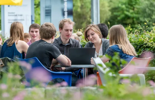 Studierende am Campus in Stade sitzen um einen runden Tisch herum draußen am Campus in Stade und schauen gemeinsam auf einen Laptop.