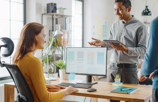 Sozialmanager nach ihrem abgeschlossenen Sozialpädagogik-Fernstudium spricht mit einem Kollegen am Schreibtisch